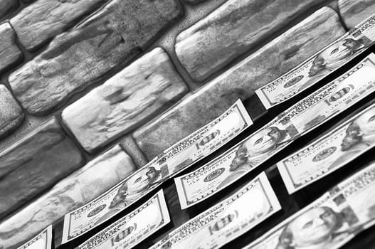 Dollars in one-hundred-dollar bills are spread out on a table near the brick wall. The dollars are arranged in a row. US dollars. On the brown brick wall there is a place for an inscription, a logo. Black and white style. Layout, template, mockup.