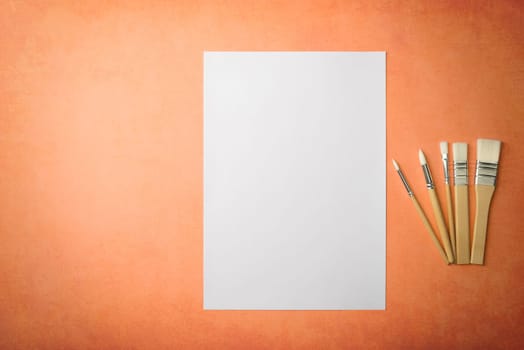A clean white sheet and brushes on a textured background with space to copy. Layout, mockup space for text and drawing.