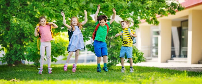 Cute children with rucksacks jumping and playing in the park near the school. Concept of elementary studying and friendship.