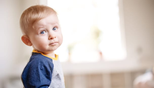 Cute boy standing in the white room. Serious baby looking at the camera. Concept of the family and mother's love.
