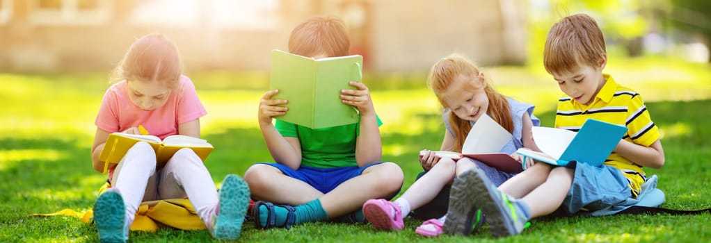 Children with rucksacks sitting in the park on the grass near the school. Pupils with books and backpacks outdoors.