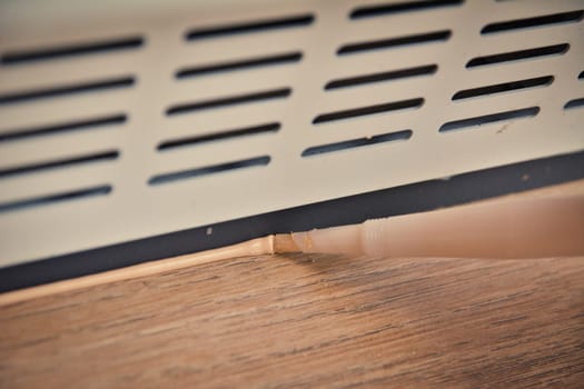 Applying brown silicone sealing on laminate flooring and plinth with ventilation grille.DIY renovation.