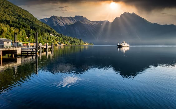 Ferry arriving on fjord during sunrise in norway with mountains in background