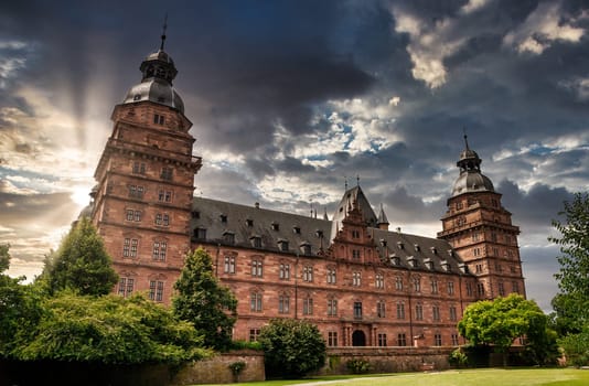Castle Johannisburg, Aschaffenburg at sunset with cloudy sky and park in forefront, Germany