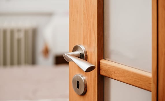 Opened modern wooden door into room, closeup detail on metal handle.