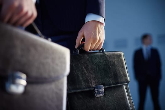 Cropped image of business partners carrying briefcases on the foreground while their colleague standing on the background