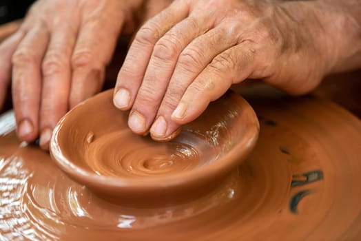Hands of the potter. The potter makes pottery dishes on potter's wheel. The sculptor in workshop makes clay product closeup