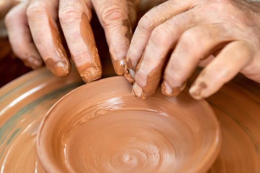 Hands of the potter. The potter makes pottery dishes on potter's wheel. The sculptor in workshop makes clay product closeup