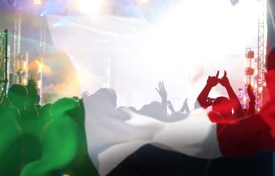 Soccer fans supporting Italy - crowd celebrating in stadium with raised hands against italian flag
