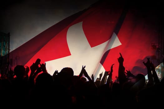Soccer fans supporting Switzerland - crowd celebrating in stadium with raised hands against Switzerland flag