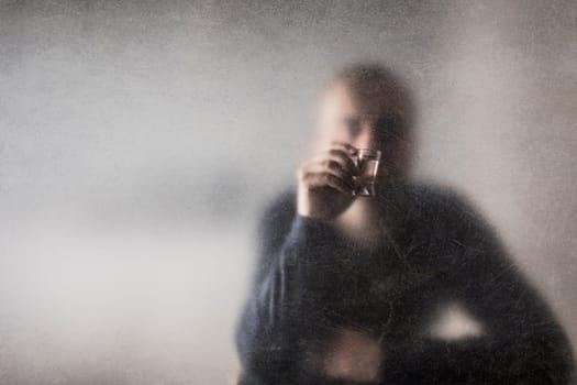Man with a glass of vodka behind a dusty scratched glass. Alcoholism concept.