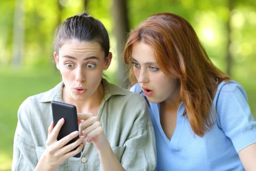 Amazed women checking phone content in a park
