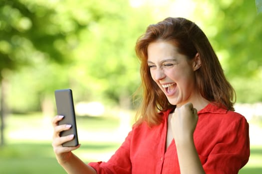 Excited woman in red celebrating checking phone