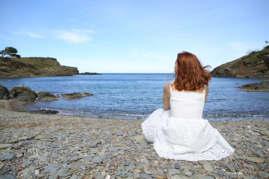 Woman in white dress sitting on the beach contemplating