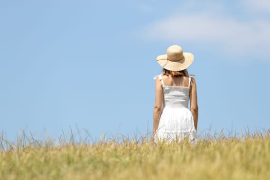 Back view of a woman walking across a wheat field