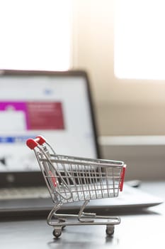 Online-Shopping concept: Miniature shopping cart, laptop and mouse in the blurry background