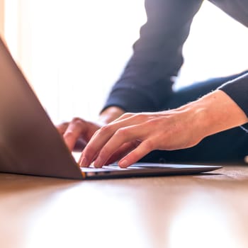 Young man with a laptop is working on the wooden floor, light comes in from the window