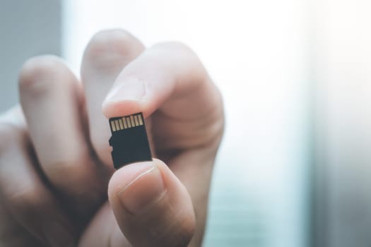 Young man is holding a tiny memory card in his hand, text space