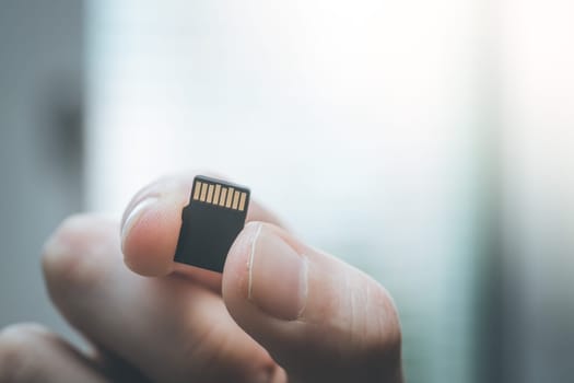 Young man is holding a tiny memory card in his hand, text space