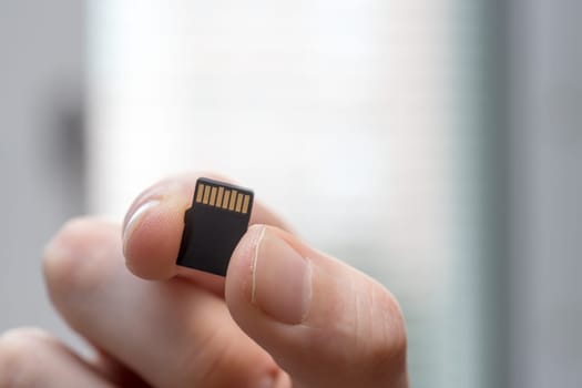Young man is holding a tiny memory card in his hand, text space