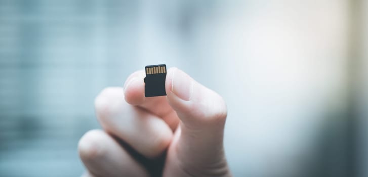 Young man is holding a tiny memory card in his hand, text space