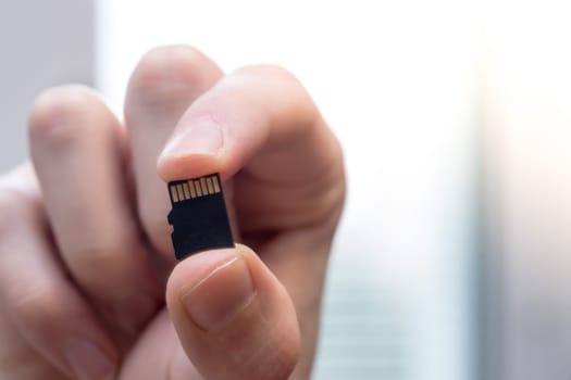 Young man is holding a tiny memory card in his hand, text space