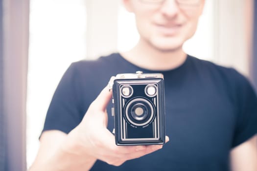 Young man in black shirt is taking a picture with a black german vintage camera