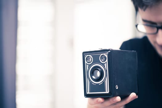 Young man in black shirt is taking a picture with a black german vintage camera