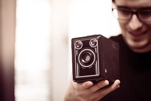 Young man in black shirt is taking a picture with a black german vintage camera