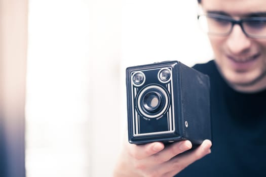 Young man in black shirt is taking a picture with a black german vintage camera