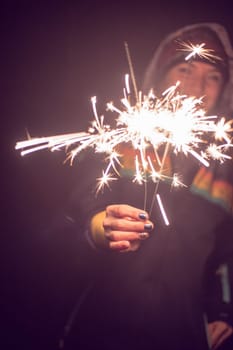 Smiling girl is holding a sparkler in her hand, new year, outdoors