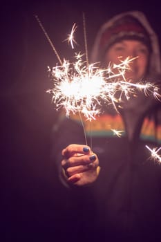 Smiling girl is holding a sparkler in her hand, new year, outdoors