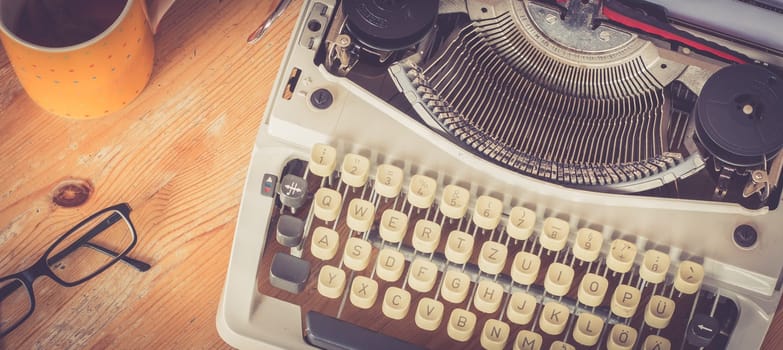 Vintage typewriter, glasses and cup of coffee on a wood desk