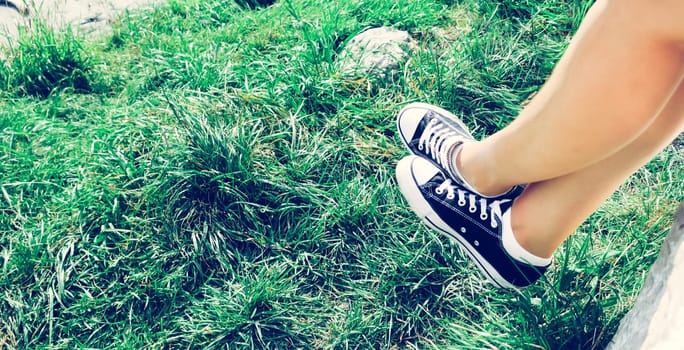 Black sneakers and green grass in the summer: free time for teenager