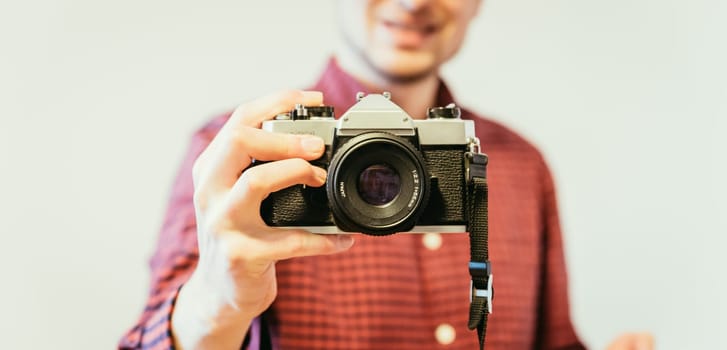 Young man in red-blue checked shirt is taking a picture with an vintage camera, retro style