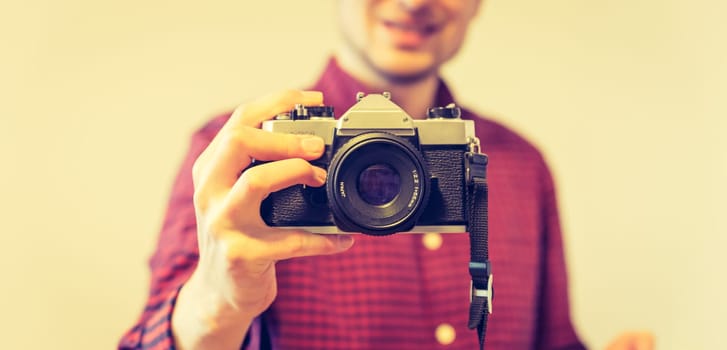 Young man in red-blue checked shirt is taking a picture with an vintage camera, retro style