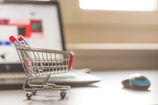 Online-Shopping concept: Miniature shopping cart, laptop and mouse in the blurry background
