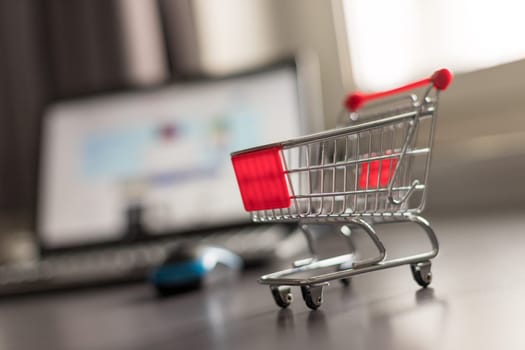 Online-Shopping concept: Miniature shopping cart, laptop and mouse in the blurry background