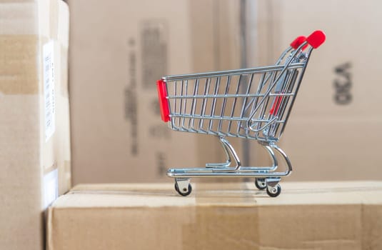 Online-Shopping and parcel service concept: Miniature shopping cart and cardboard boxes