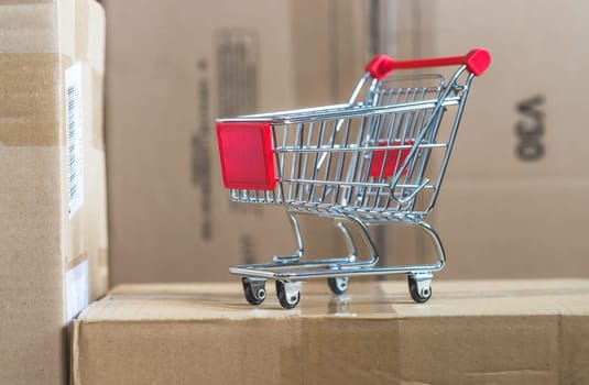 Online-Shopping and parcel service concept: Miniature shopping cart and cardboard boxes
