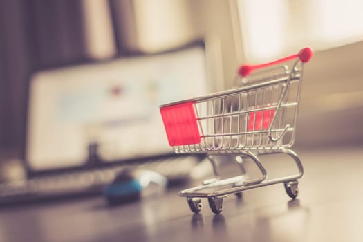Online-Shopping concept: Miniature shopping cart, laptop and mouse in the blurry background