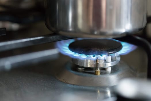 Close up of a blue gas flame, cooking a water pot in kitchen