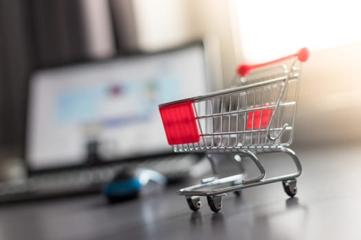 Online-Shopping concept: Miniature shopping cart, laptop and mouse in the blurry background