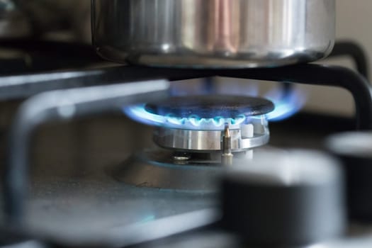 Close up of a blue gas flame, cooking a water pot in kitchen