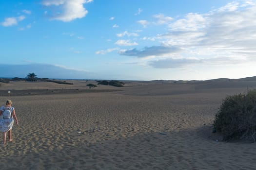 Woman in dress walking in the sand of desert dunes with steps in the desert sand, young woman walking in white sand on a bright summer day, holiday vacation concept