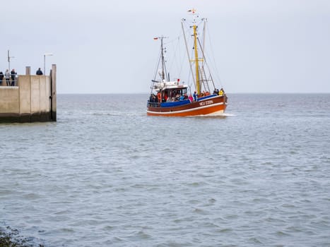 View of the harbor wall at the entrance to Harlesiel in East Freeland with the incoming excursion fishing trawler when the sky is overcast.