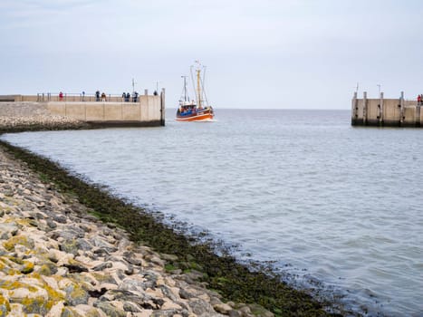 View of the harbor wall at the entrance to Harlesiel in East Freeland with the incoming excursion fishing trawler when the sky is overcast.