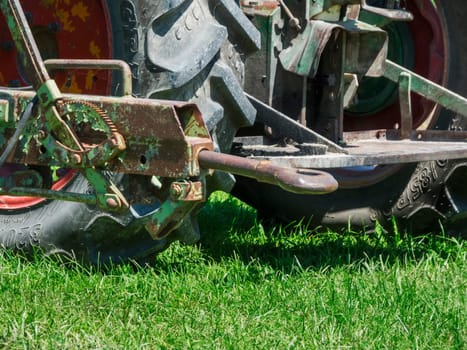Detailed view of an outdated, rusty and bent trailer coupling on a tractor in front of a rough tire tread on a lawn