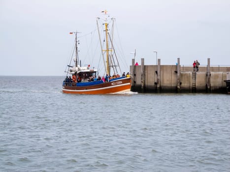 View of the harbor wall at the entrance to Harlesiel in East Freeland with the incoming excursion fishing trawler when the sky is overcast.