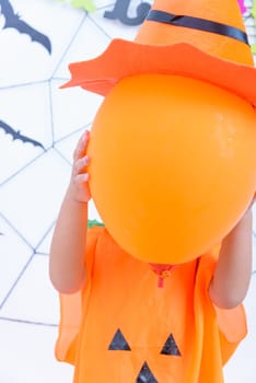 Funny happy kid boy in Halloween costume with Jack and have orange balloon on hand with Cobweb on background